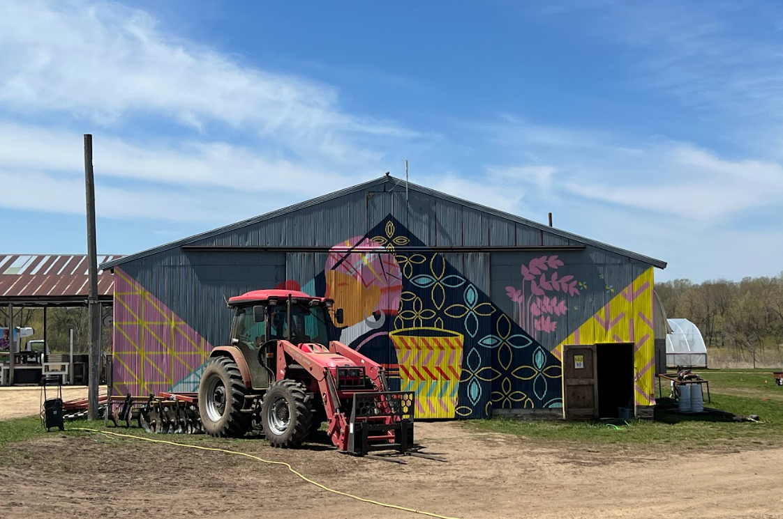red tractor in front of blue sky and farmhouse with paintings on it