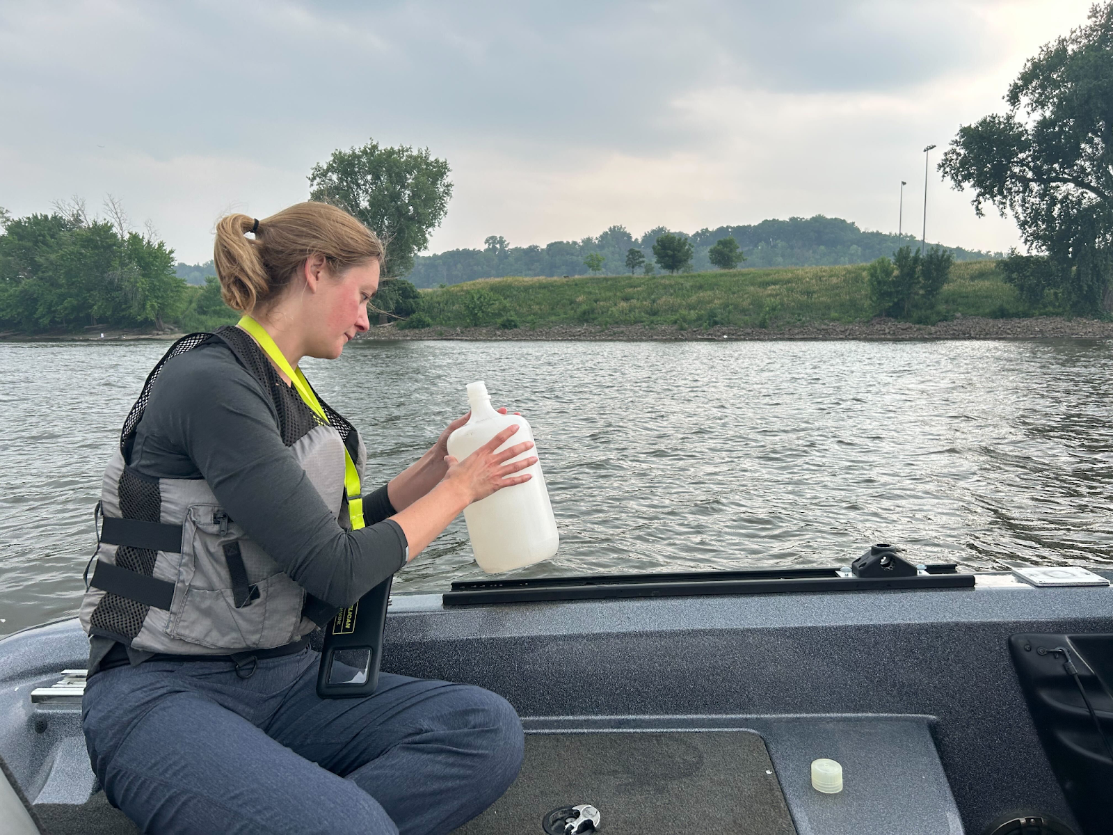 a white woman in a boat wears a life jacket and holds a jug with a water sample in it