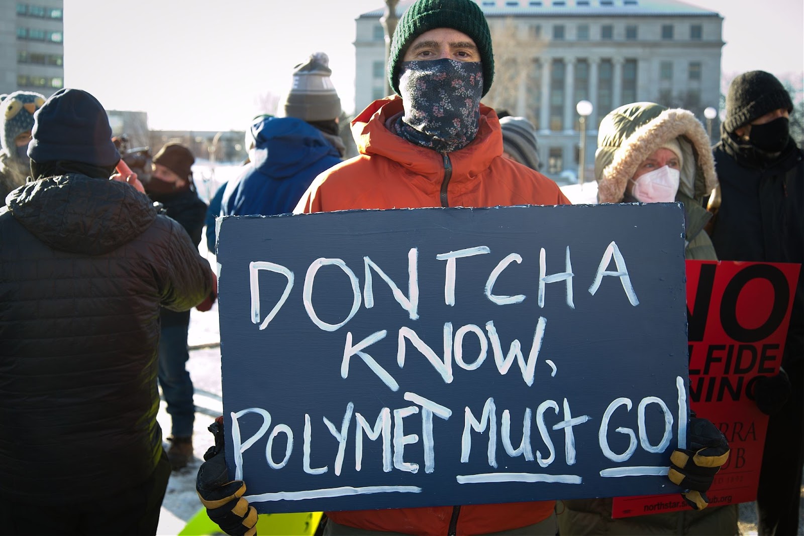 jay eidsness stands holding a sign that says doncha know polymet must go
