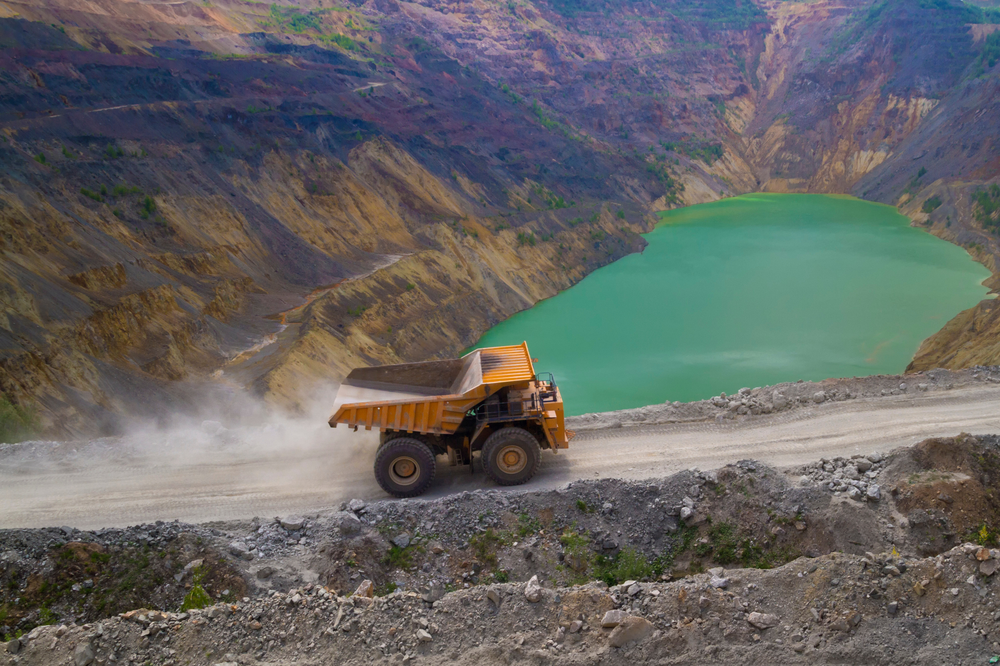 Dump truck driving up mine pit with blue pool in background
