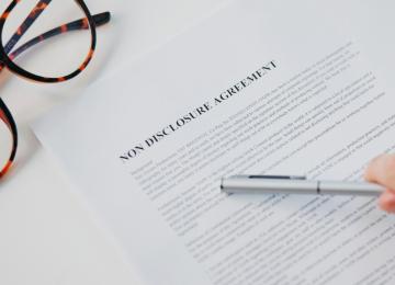 a document that says non disclosure agreement, a white hand holding a pen, and a pair of glasses