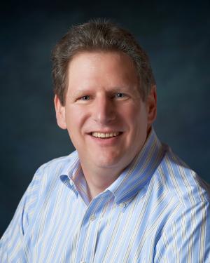 photo of a smiling white man in a blue button down shirt