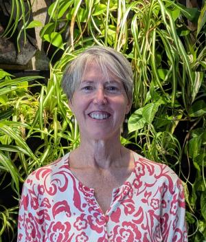 a photo of a smiling white woman in a floral shirt standing in front of plants