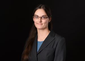 a white woman with long hair in a dark suitcoat standing in front of a dark background