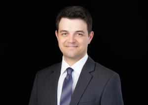 a photo of a smiling white man in a blue tie against a black background
