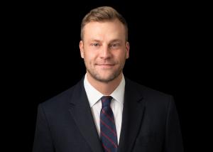 a white man in a dark suit in front of a dark background