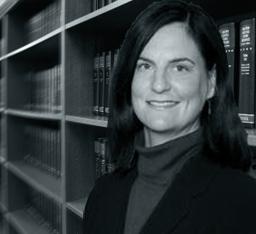Bridget Hust. White woman standing in front of bookshelf full of law books.