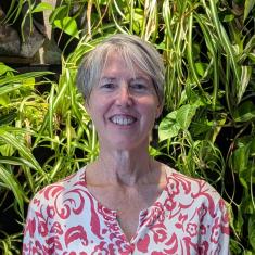 a photo of a smiling white woman in a floral shirt standing in front of plants