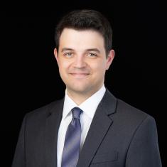 a photo of a smiling white man in a blue tie against a black background