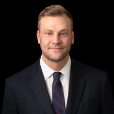 a white man in a dark suit in front of a dark background