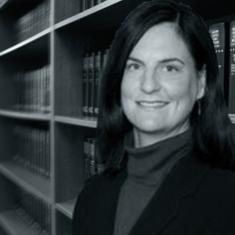 Bridget Hust. White woman standing in front of bookshelf full of law books.