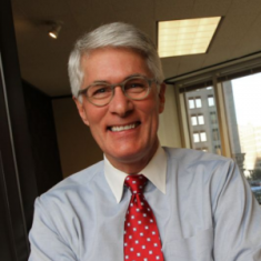 Photo of Alan Thometz. White man with white hair wearing button down dress shirt and tie, in an office.