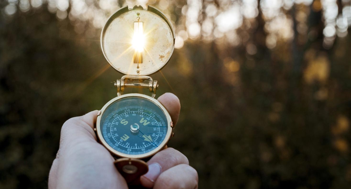 a white hand holding a compass in the woods