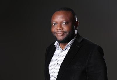 a photo of eric ini, a Black man standing in a suit in front of a dark background