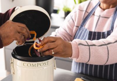 two people put orange peels into a compost bucket