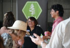 photo of MCEA staff member speaking to supporters at Duluth event with M C E A logo in background