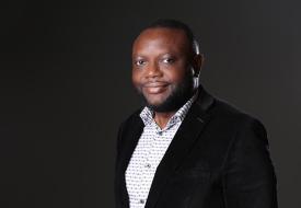 a photo of eric ini, a Black man standing in a suit in front of a dark background