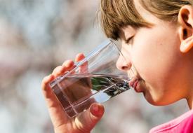 a white girl with brown hair and pink shirt drinks a glass of water