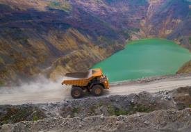 Dump truck driving up mine pit with blue pool in background