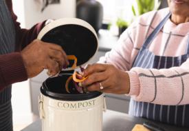 two people put orange peels into a compost bucket