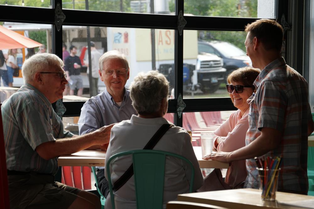 photo of a group of MCEA supporters seated at a table interacting with a standing M C E A staff member