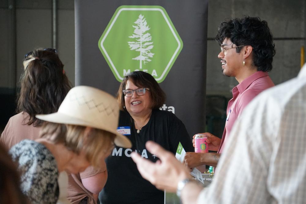 photo of MCEA staff member speaking to supporters at Duluth event with M C E A logo in background